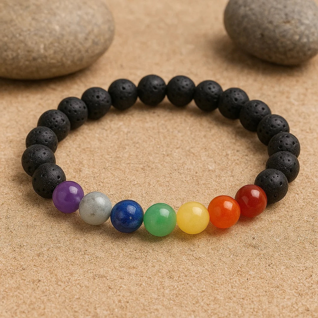 7 Chakra bracelet made with colorful gemstone beads and black lava stones placed on sand background.