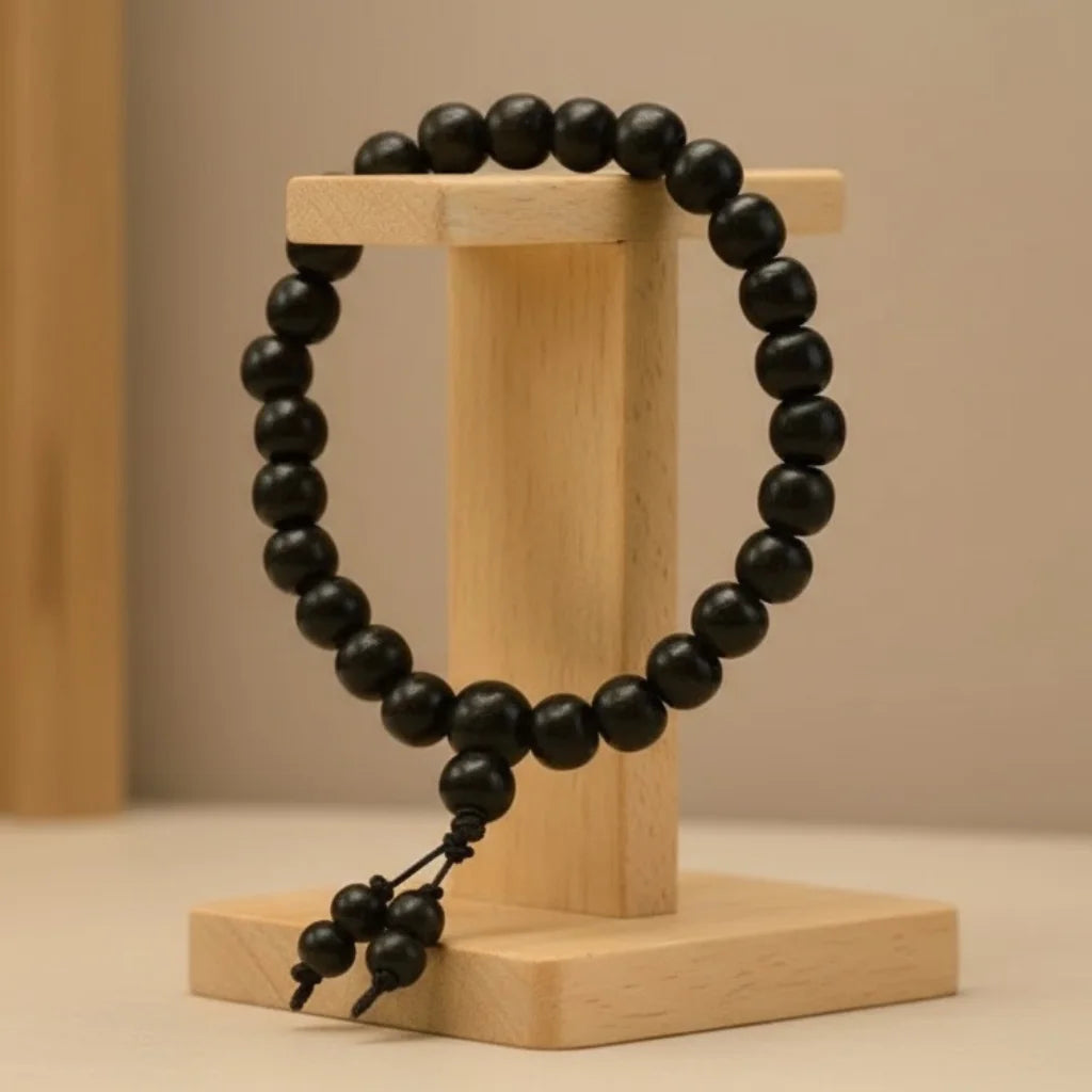Black beaded karungali bracelet on a wooden stand against a beige background