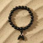 Black beaded karungali bracelet with a pendant on a sandy background