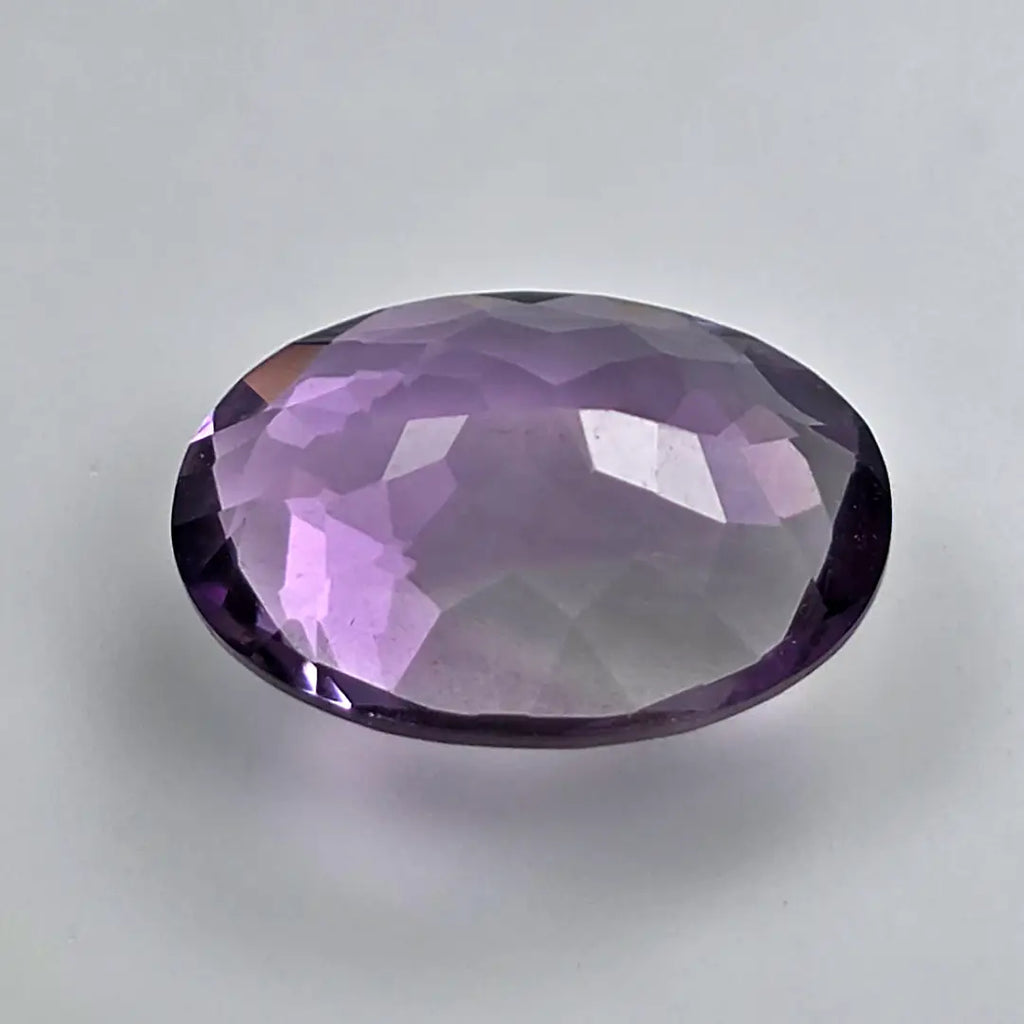 Faceted purple amethyst gemstone on a light grey background