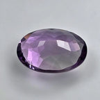 Faceted purple amethyst gemstone on a light grey background