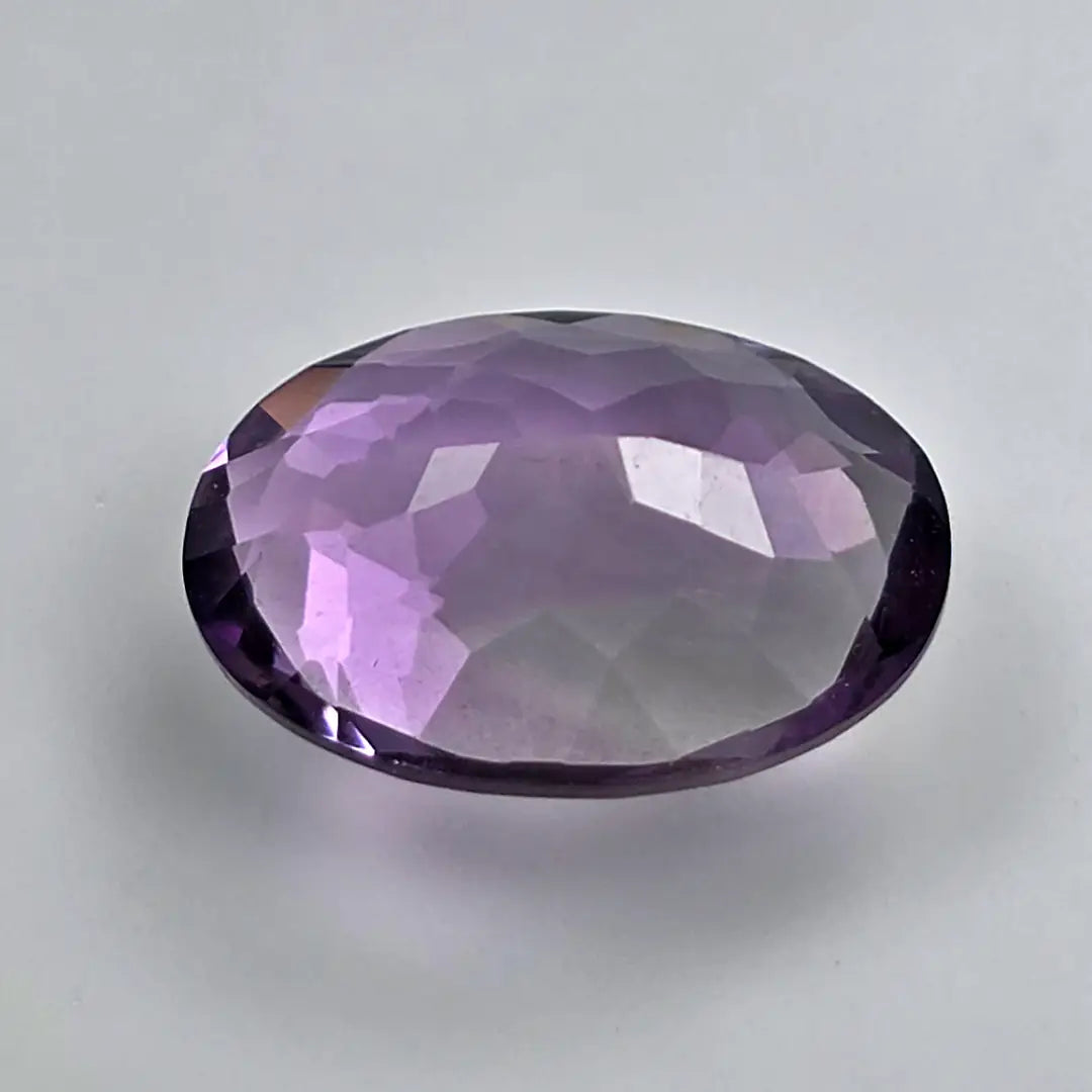 Faceted purple amethyst gemstone on a light grey background