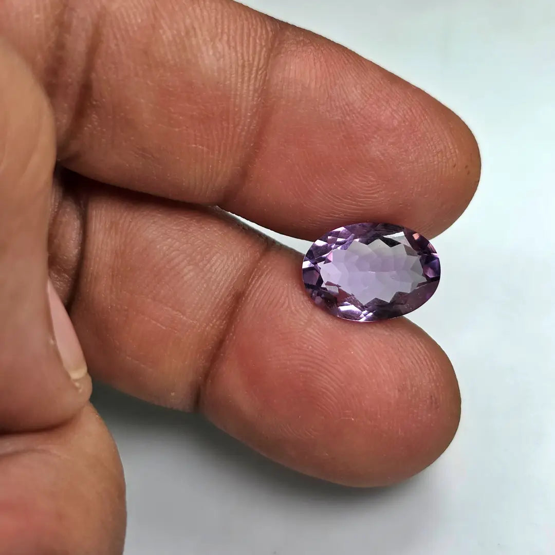 Purple amethyst gemstone held between fingers on a light background