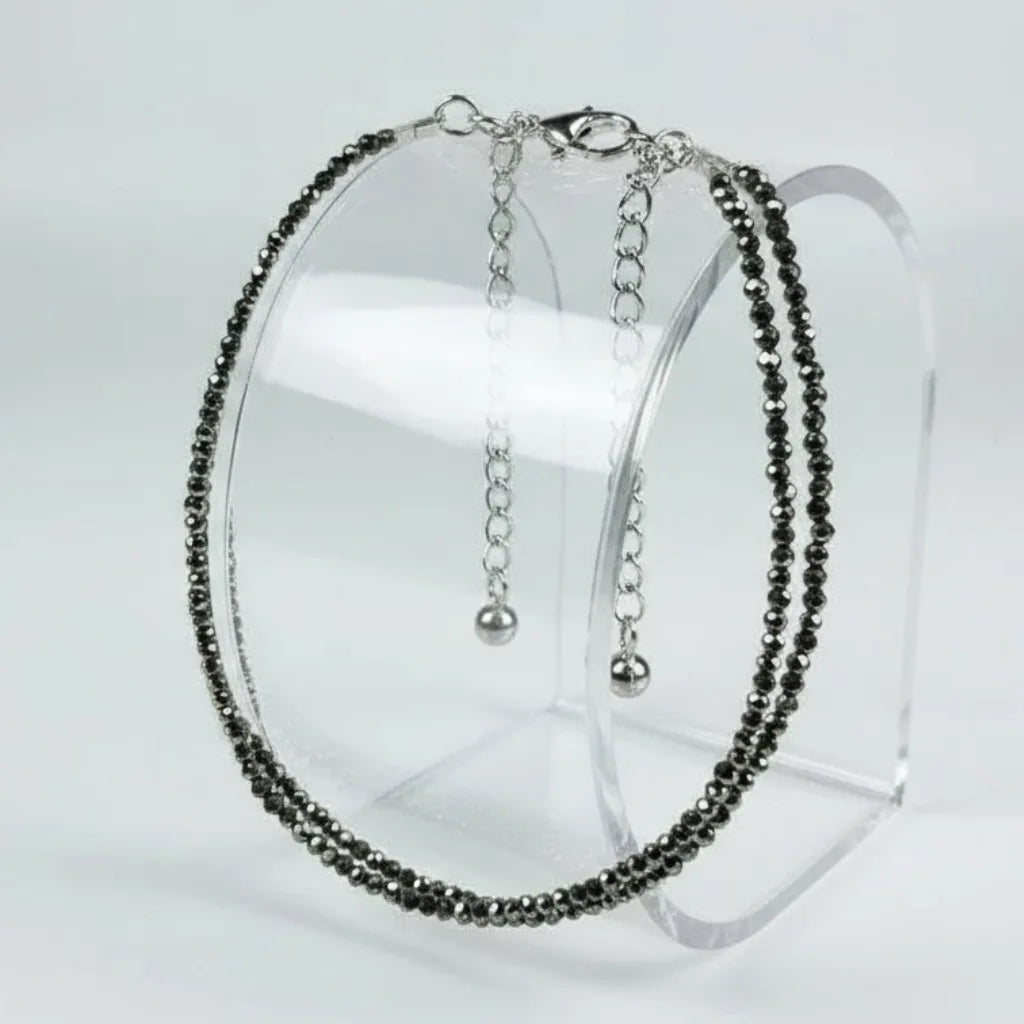 anklet with black beads and silver chain on a clear stand against a white background