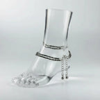 Clear glass foot with silver anklets on a light gray background