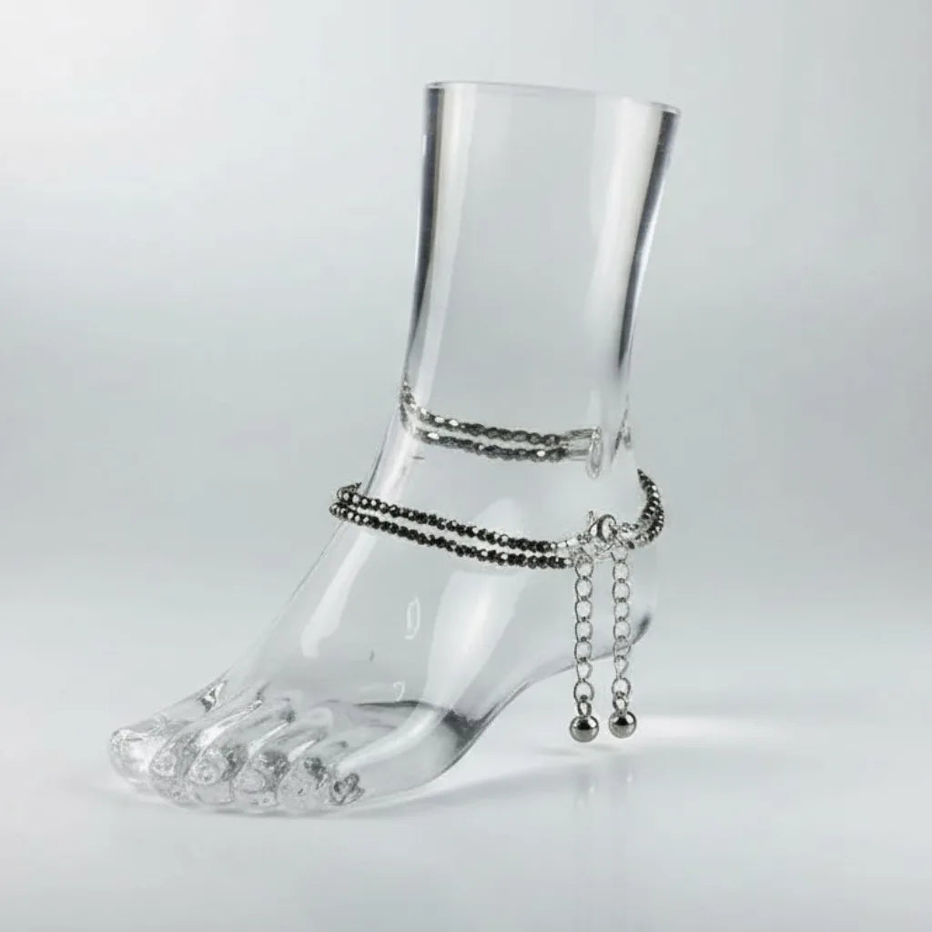 Clear glass foot with silver anklets on a light gray background