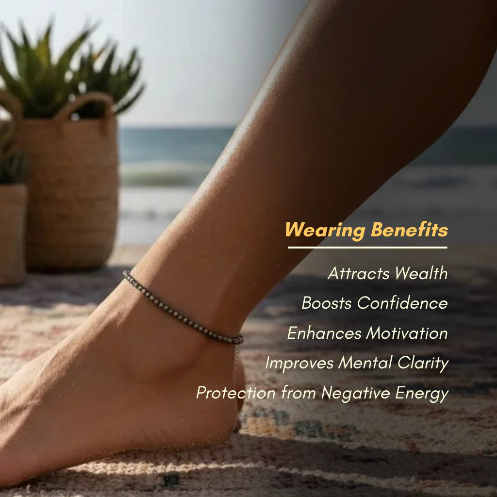 Person's foot wearing a bracelet with beach and plants in the background