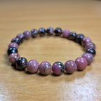 Beaded rhodonite bracelet with pink and black beads on a wooden surface