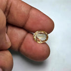 Hand holding a yellow citrine gemstone against a white background
